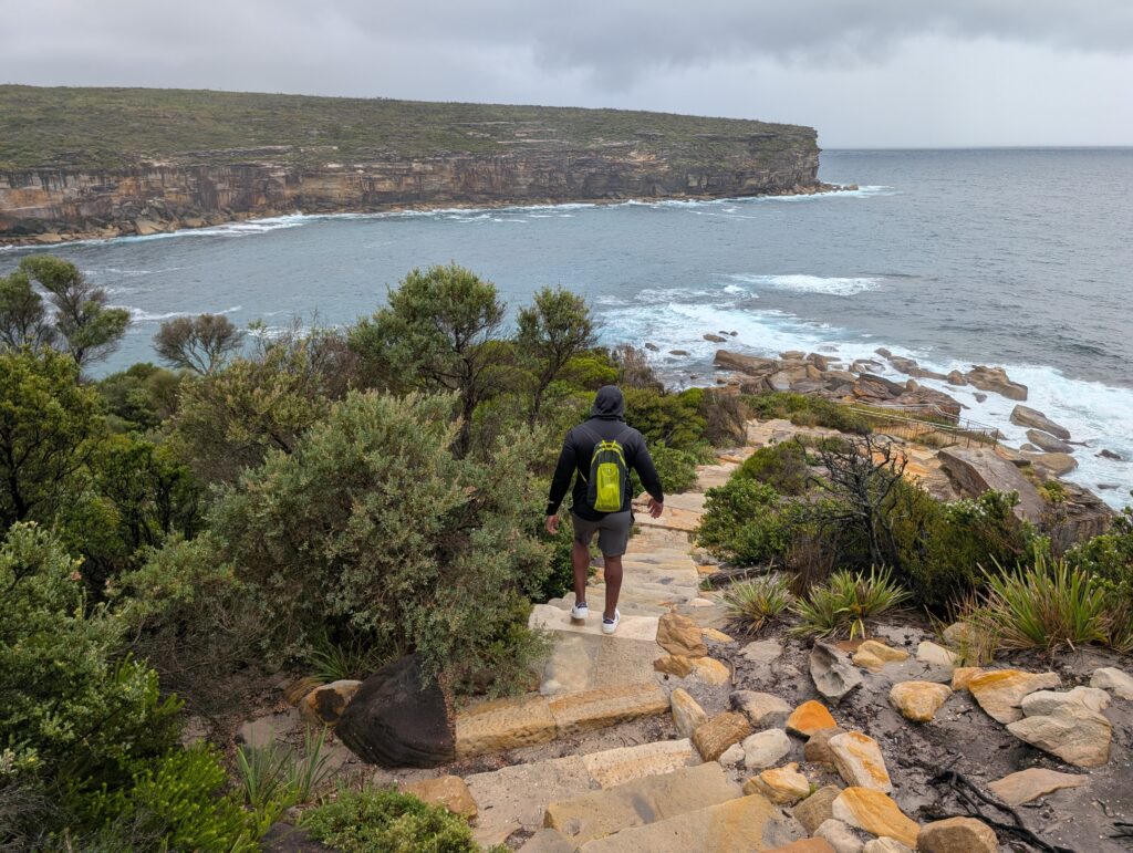 A man descending a stone staircase towards an inlet of water on a cloudy day
