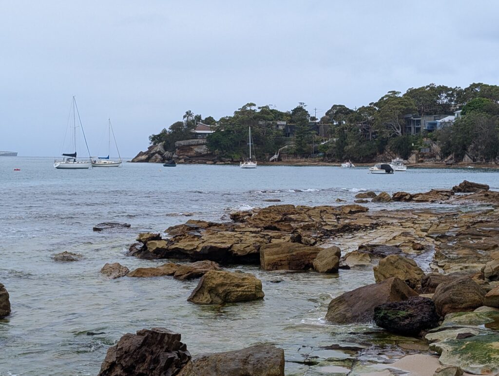 A rocky shoreline with sail boats in the distance on a cloudy day
