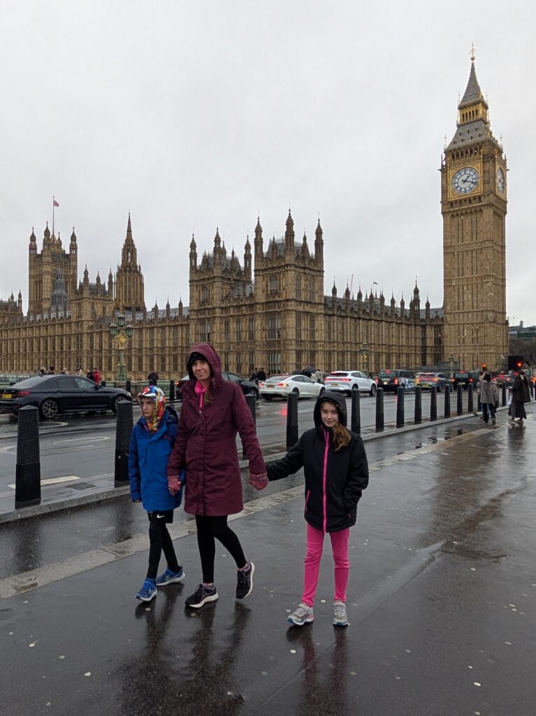 A mother and two children on a sidewalk with Big Ben and the Parliament building behind them