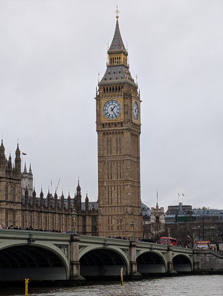 A zoomed in view of Big Ben with a bridge and water in the foreground
