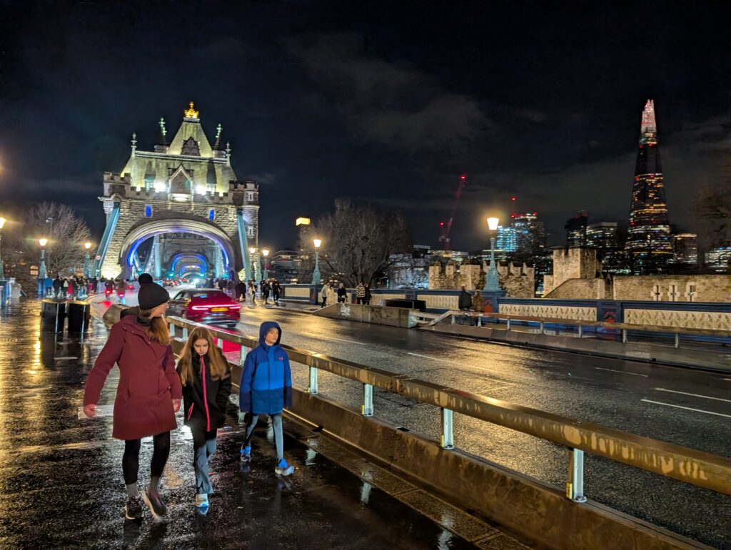A mother and children walking alongside a road that leads to a lit-up bridge in London