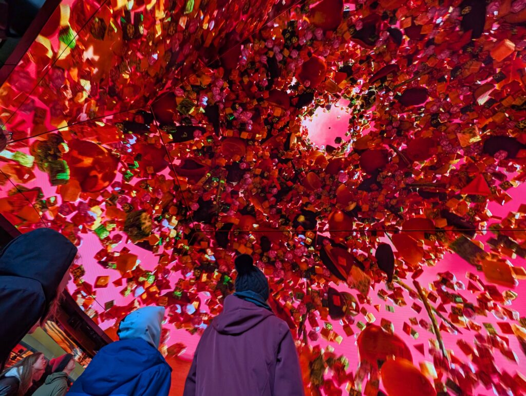 Three people looking up at a screen that shows tons of red balloons that appear to be floating up