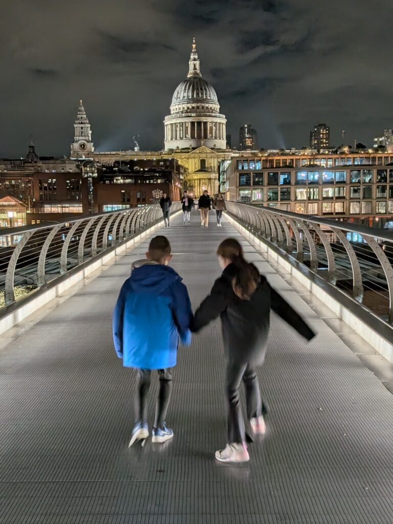 Two young children on a gray bridge that leads to a giant cathedral at night