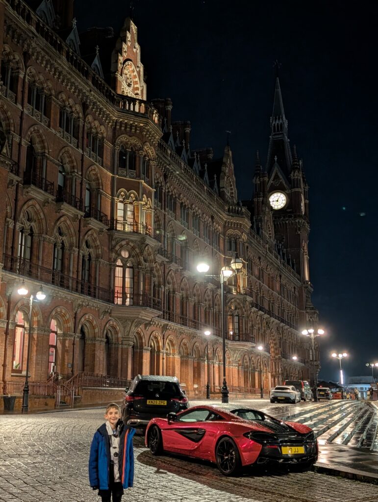 A boy in front of a sports car with a large gothic building in the background at night
