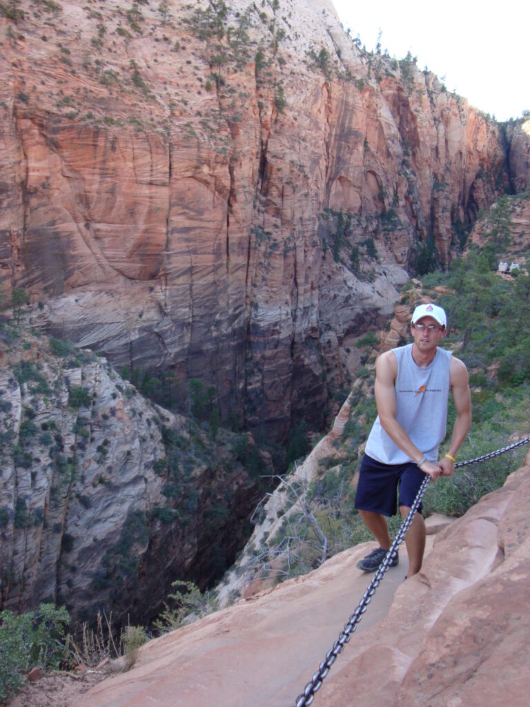 A man holding on to a chain with both hands while standing on the edge of a rocky ledge