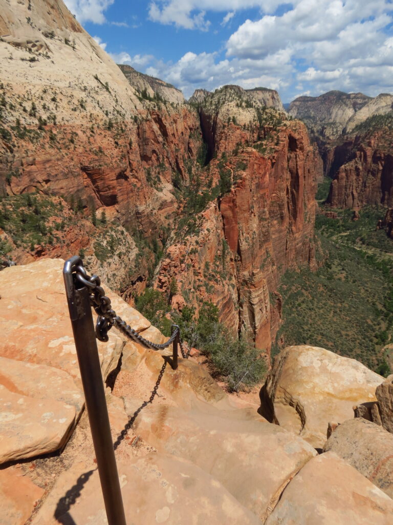 A pole holding a chain in the foreground leading down a rocky trail high above a canyon