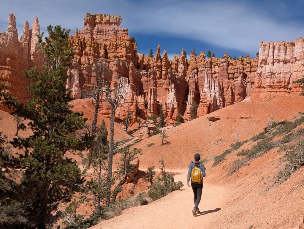 A hiker walking along a sandy path with orange and white rocks at Bryce Canyon
