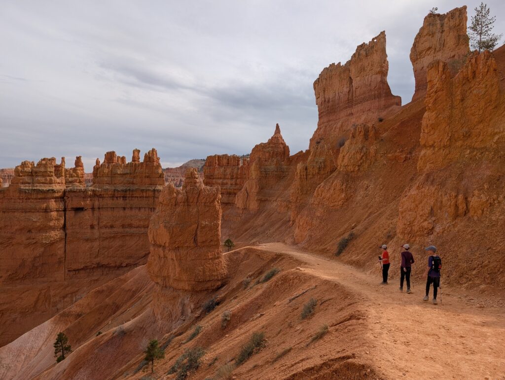 Three young boys stand on a hiking trail with an orange wall of spires in the background