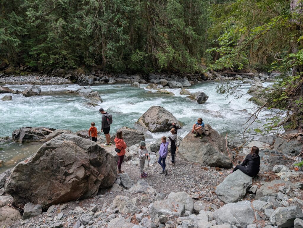 A group of adults and kids at the edge of a running river