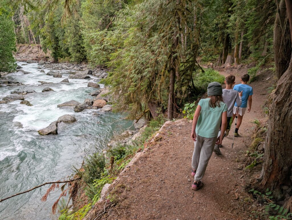Several kids along a dirt hiking path next to a river