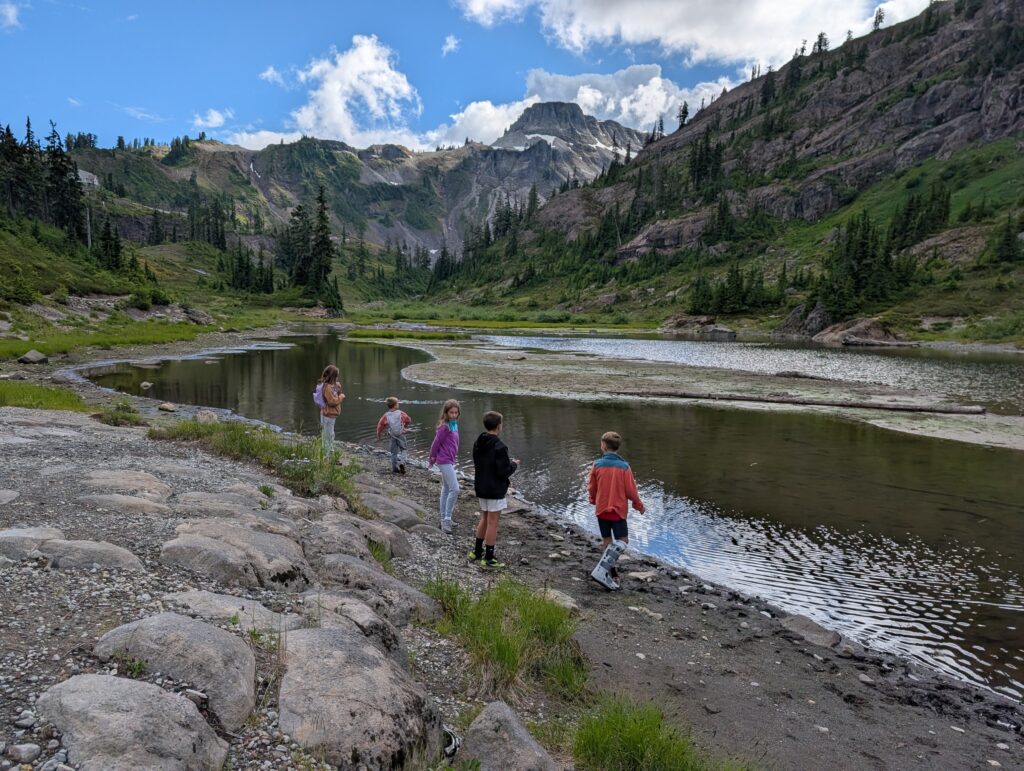 Children standing along the edge of a small body of water surrounded by mountains
