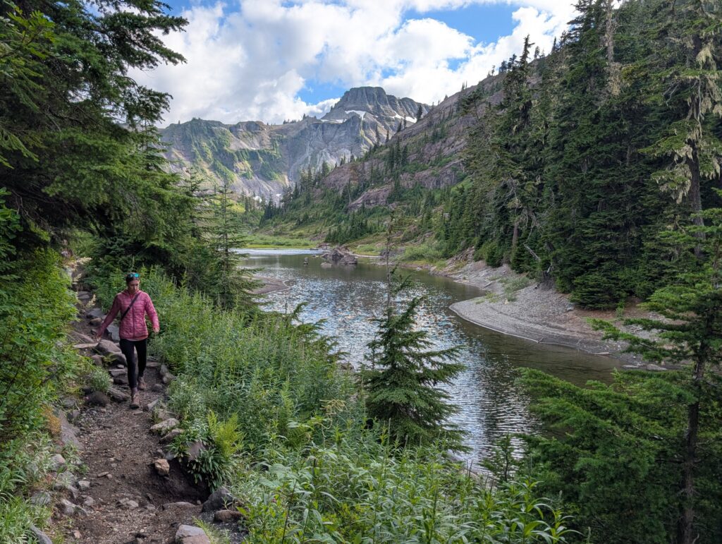 A woman hiking on a dirt path next to a body of water with mountains far off in the distance
