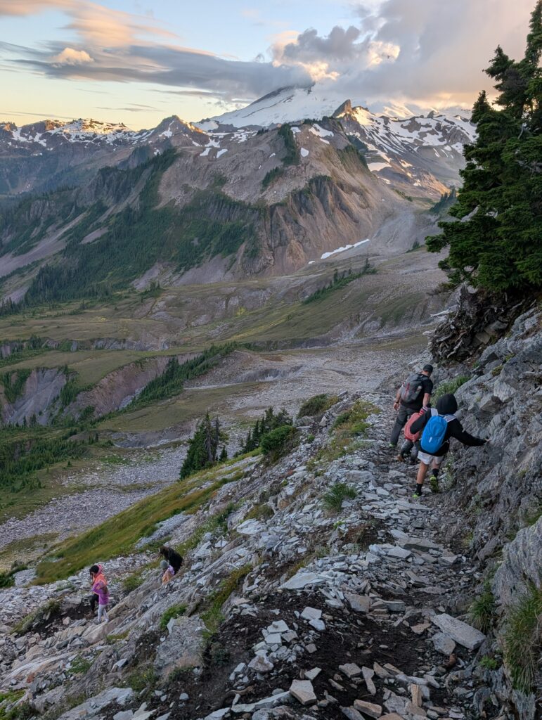 Several hikers on a narrow rocky path with a large mountain in front of them