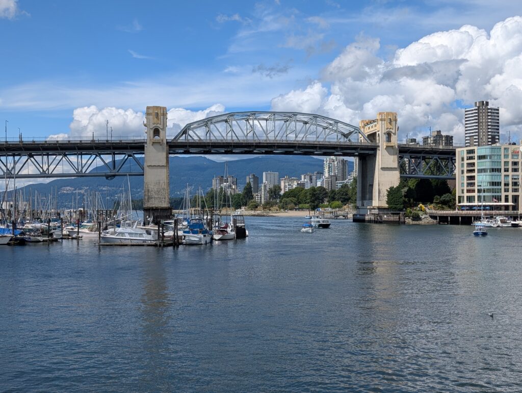A car bridge over a body of water with boats and mountains in the background