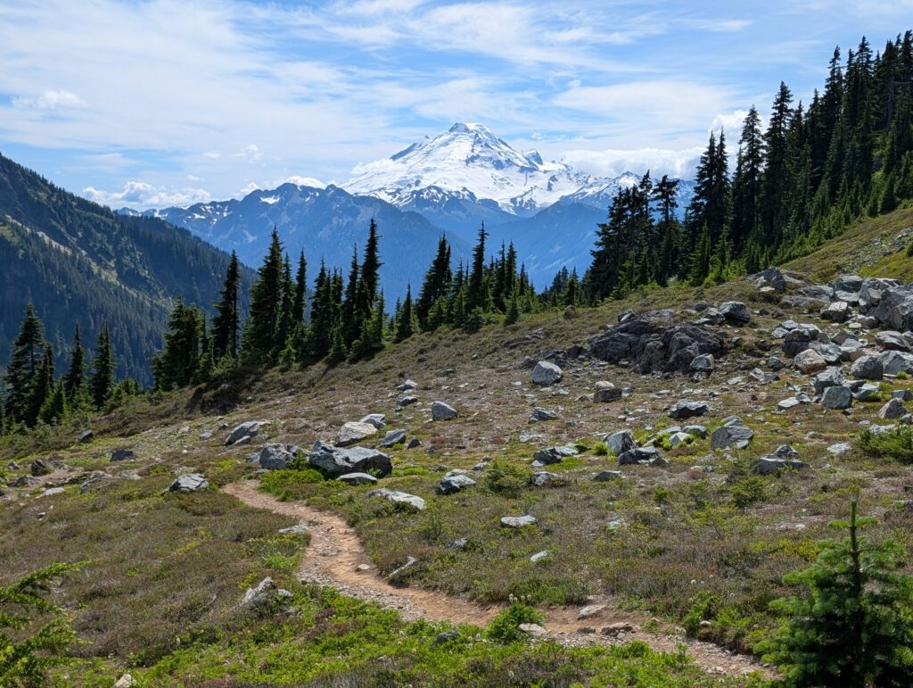 A dirt path winding through the foreground with a towering snow-covered single mountain peak in the background