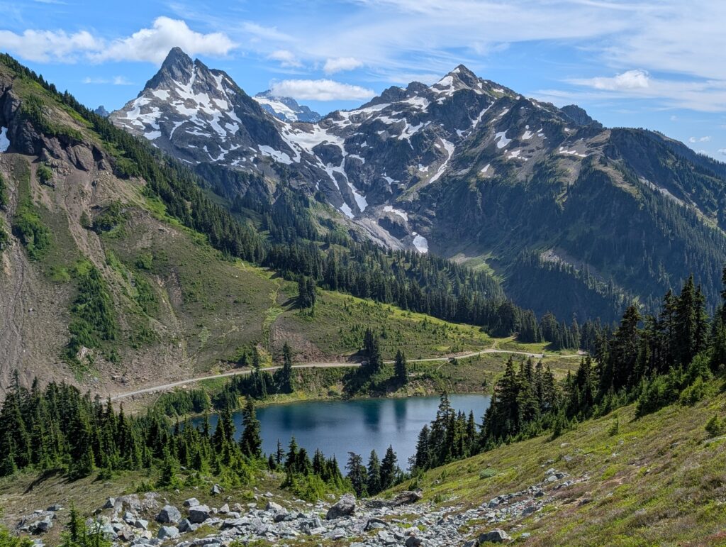 A small lake below jagged mountains covered with some snow