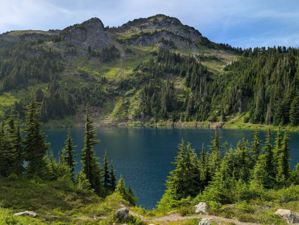 A blue lake below a couple mountain peaks with trees and grass all around