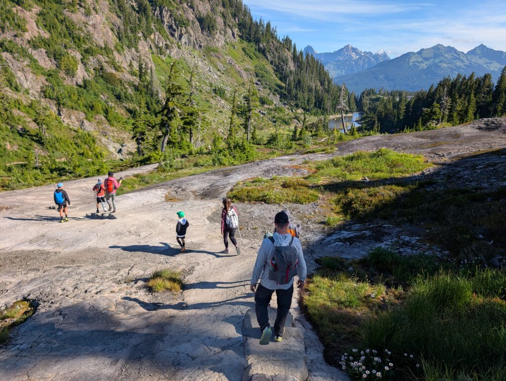 A group of hikers walking down a smooth rock path with trees and mountains