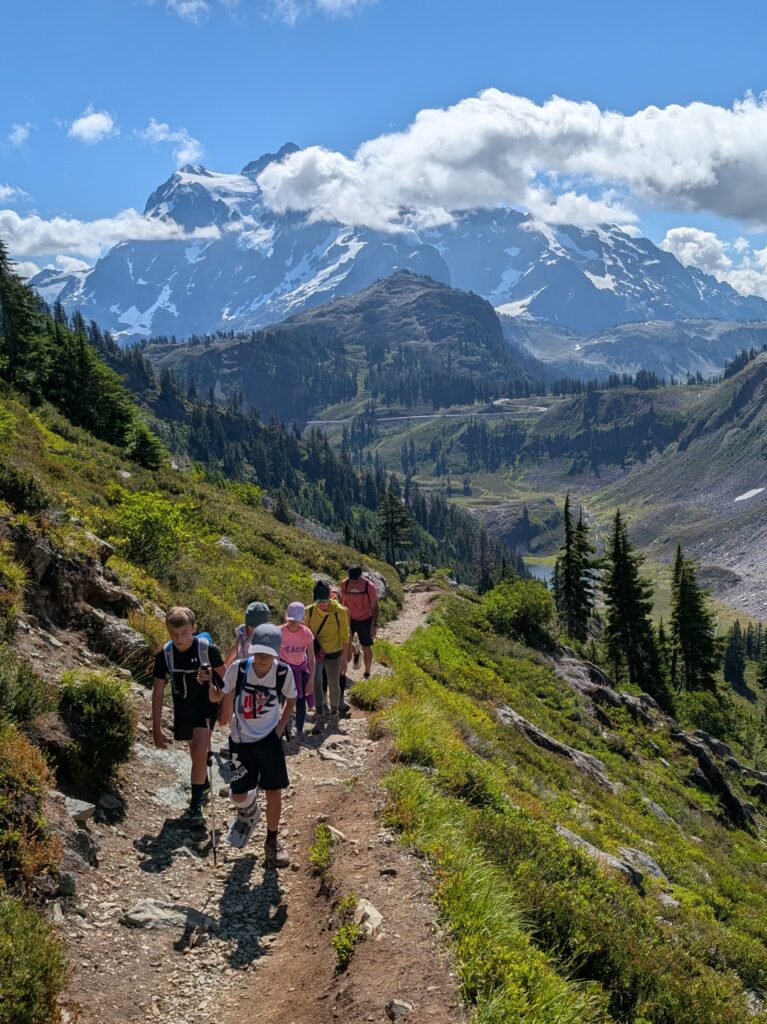 A group of hikers walking forward with a large mountain formation somewhat obscured by clouds