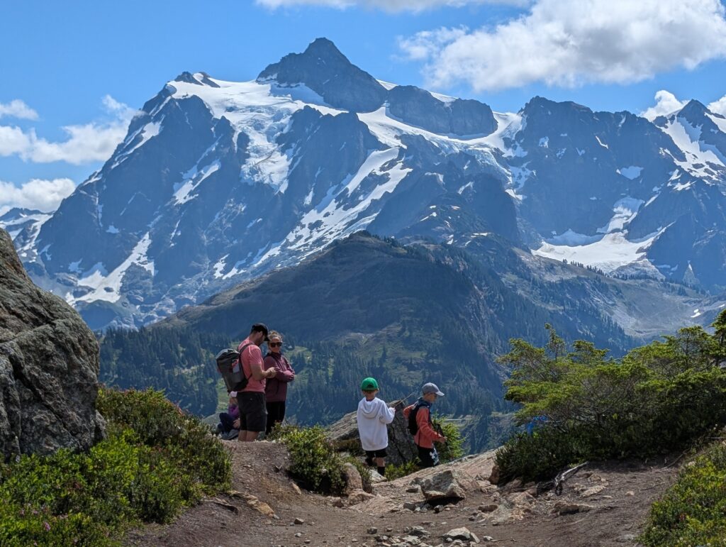 A zoomed-in gigantic mountain face behind a family on the Chain Lakes Loop trail