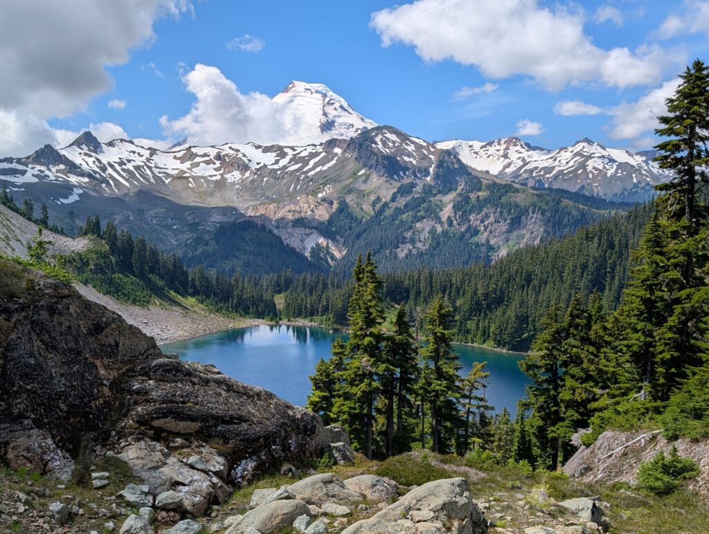 A blue-green lake surrounded by trees with a mountain centered in the background