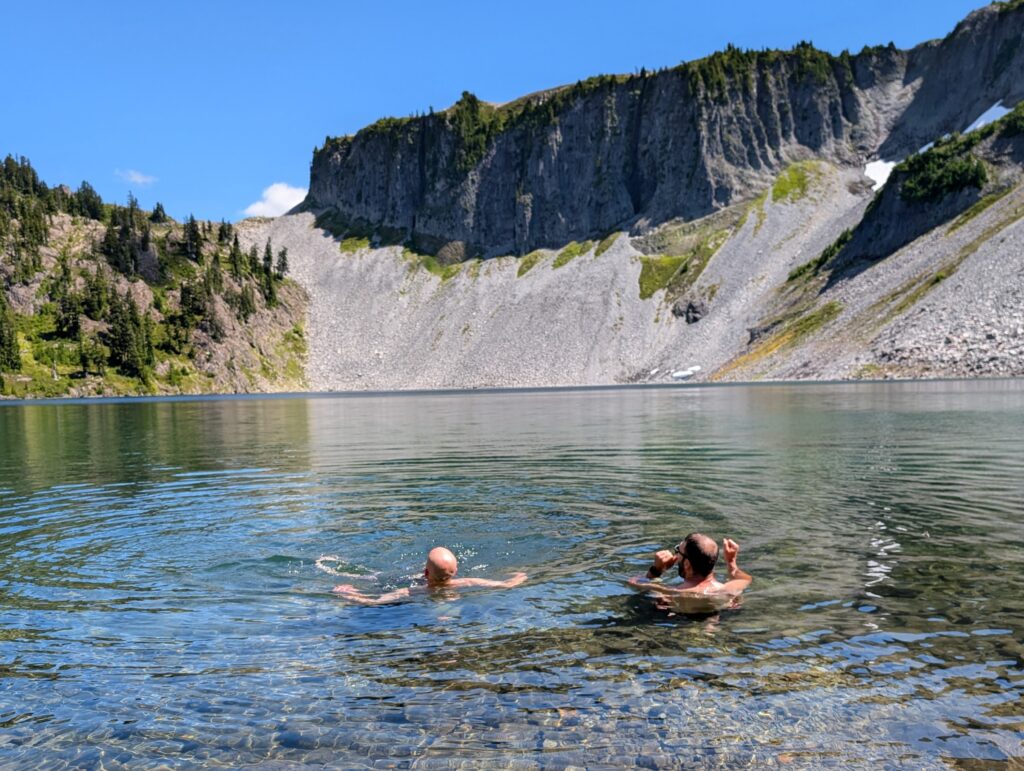 Two men sitting in water up to their necks looking out at a flat-topped mountain formation