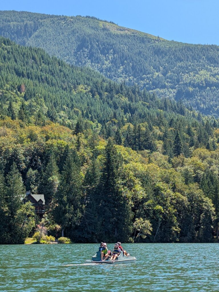 A paddleboat in the middle of a body of water with rising forest-covered hills in the background